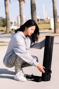 young asian woman dressed in sportswear preparing her mat for a yoga session outdoors, healthy and active lifestyle concept