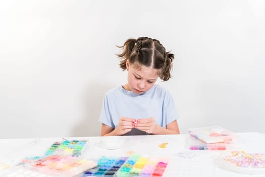 Little girl enjoys crafting colorful bracelets with vibrant clay beads set.