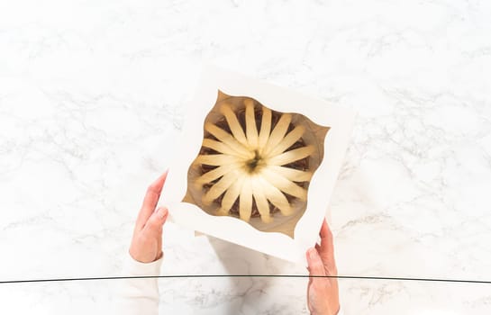 Flat lay. The freshly baked bundt cakes are carefully nestled into white paper boxes, preparing them for secure transportation while maintaining their delectable appearance.