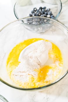 Integrating ingredients in a glass bowl, adeptly stirring with a whisk to craft a tantalizing lemon-blueberry bundt cake.