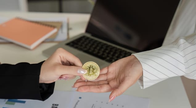 Two businesswomen hand each other cryptocurrency coins. Cryptocurrency exchange concept.