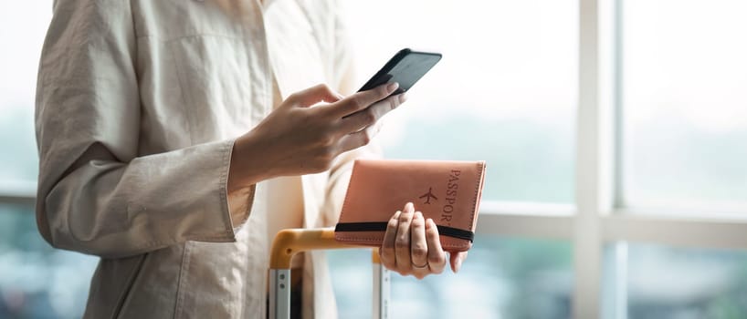 Tourist woman using mobile smartphone and holding passport with suitcase traveling between waits for flight in Airport Terminal, flight check in, Tourist journey trip concept.