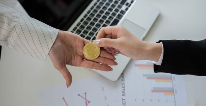 Two businesswomen hand each other cryptocurrency coins. Cryptocurrency exchange concept.