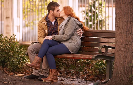 Couple, love and sitting with kiss at park in cold weather or winter, together and support in London. Relationship, commitment and bonding for romance with soulmate, care and happiness with affection.
