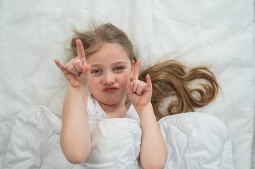 Top view of a grimacing little girl lying in bed