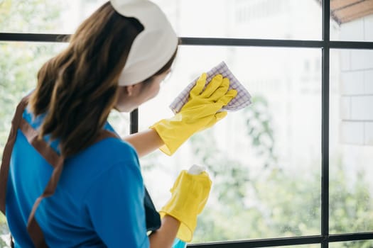 With a cheerful demeanor a young woman diligently cleans office windows using spray and cloth. Her housework emphasizes purity hygiene and transparent cleanliness.