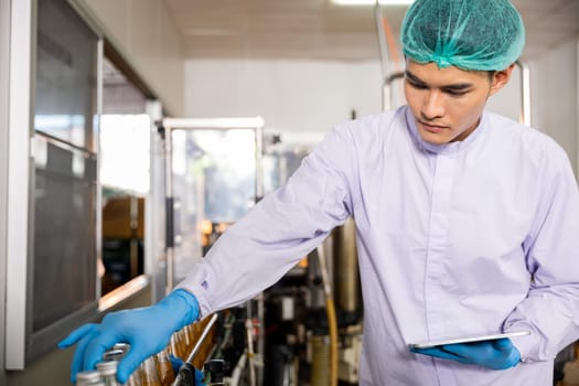 Inspecting the beverage bottling factory a quality control officer ensures line efficiency with a tablet. The machinery engineer checks and maintains machines for basil or chia seed bottle production.