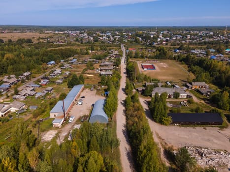 Drone view of roadway between trees and dwelling buildings under cloudy blue sky in region of Kirov Russia