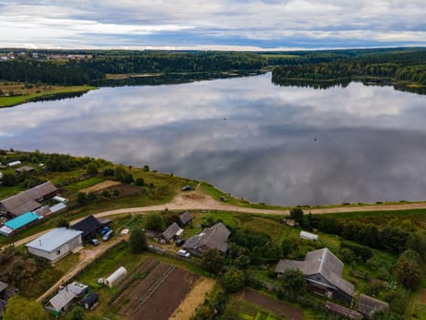 Majestic aerial view of small settlement located on shore of calm lake reflecting sky in summer