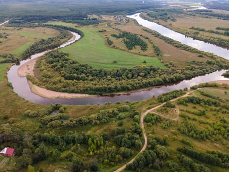 Drone view of river between curved roadway and meadows with lush green trees in region of Kirov Russian Federation