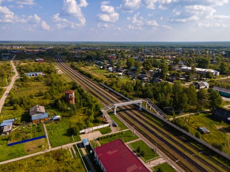 From above of railways and bridge between lush trees and dwelling buildings under cumulus clouds in region of Kirov Russia