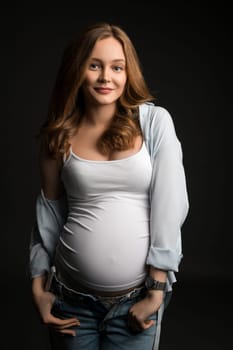 Young pregnant female in casual clothes standing on dark background and looking at camera