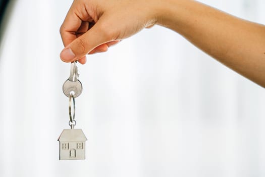 Hand holds key to house marking homeowners' achievement. Agent presents model home symbolizing real estate success. Confidence and happiness resonate.