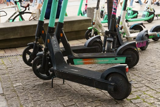 Warsaw, Poland - August 6, 2023: A group of parked electric scooters available for rent, with one scooter lying on its side on a cobblestone sidewalk.