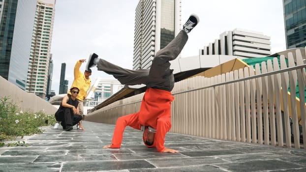 Young happy hipster perform break dancing or foot step with friend moving to hiphop music together. Skilled dancer doing freeze pose and waving hand. Modern lifestyle. Outdoor music 2024. Sprightly.