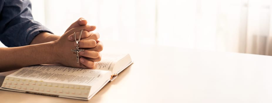 Asian male folded hand prayed on holy bible book while holding up a pendant crucifix. Spiritual, religion, faith, worship, christian and blessing of god concept. Blurring background. Burgeoning.