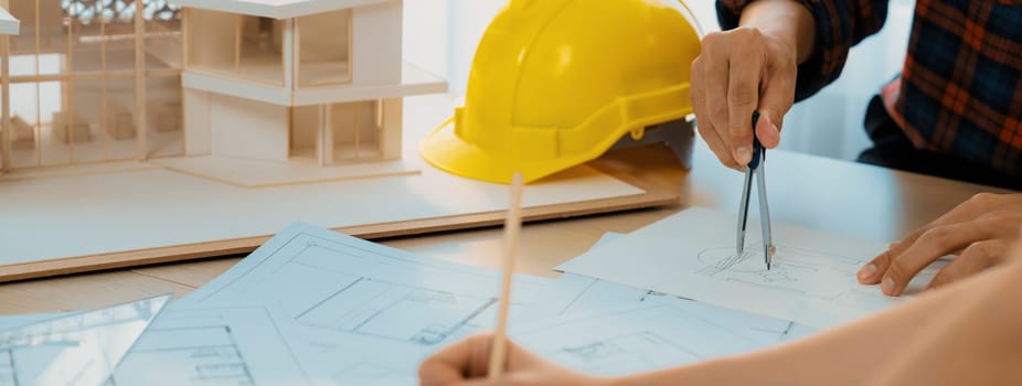 Cropped image of cooperative architect team decide and work together on meeting table with house model, safety helmet and architectural plan scatter around. Closeup. Focus on hand. Burgeoning.