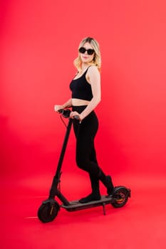 Blonde woman on red white background sitting on an electro scooter and resting, copy space