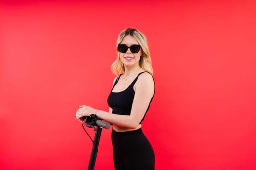 Blonde woman on red white background sitting on an electro scooter and resting, copy space