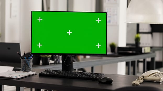 Empty office desk with pc running greenscreen on display, showing isolated chromakey template in coworking space. Workstation in open floor plan with monitor and copyspace layout.