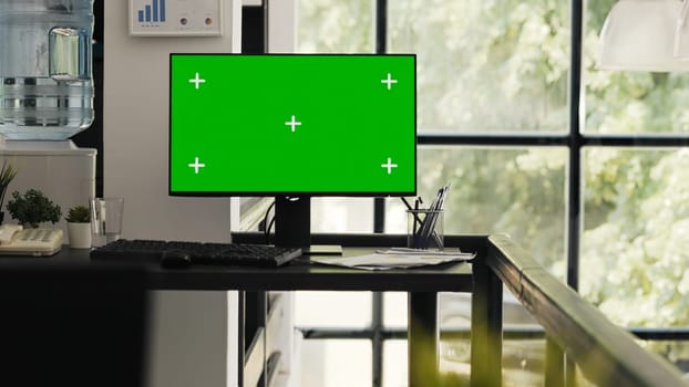 Empty office with greenscreen desktop showing isolated copyspace layout in open floor plan coworking space. Workstation desk with computer monitor presenting blank mockup screen.