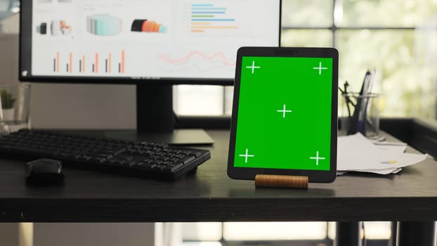 Workstation with greenscreen on tablet in agency coworking space, running isolated chromakey template on mobile device display. Empty office desk showing gadget with blank copyspace layout.
