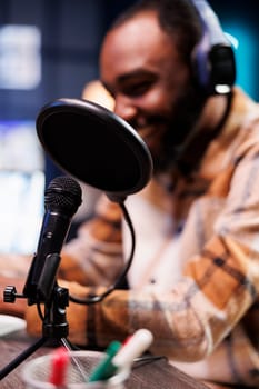 Closeup of joyful black man creating a vlog for subscribers using professional podcast microphone. On air online production, male host, broadcasting live social media content with audio equipment.
