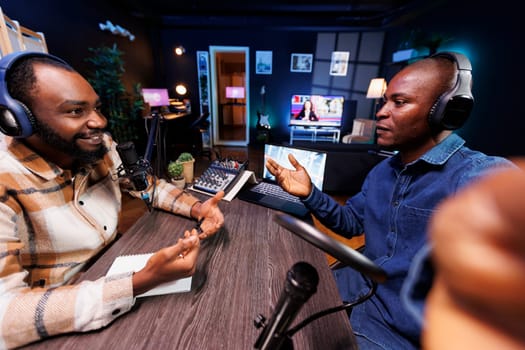 African man holding smartphone and recording podcast episode for online audience. Content creators selfie camera and audio equipment when making live talk show for their social media page.