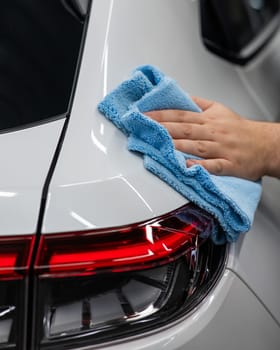 A mechanic wipes the body of a white car with a microfiber cloth