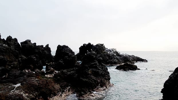 Dramatic view of sharp volcanic rocks against the calm sea under a hazy morning sky