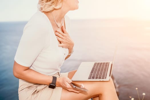 Digital nomad, Business woman working on laptop by the sea. Pretty lady typing on computer by the sea at sunset, makes a business transaction online from a distance. Freelance remote work on vacation