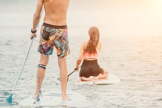 Sea woman and man on sup. Silhouette of happy young woman and man, surfing on SUP board, confident paddling through water surface. Idyllic sunset. Active lifestyle at sea or river