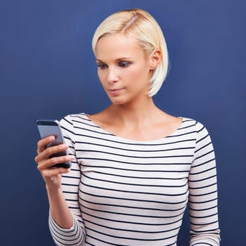 Woman, typing and browsing with phone for social media, communication or networking on a blue studio background. Female person or blonde on mobile smartphone for online chatting or texting on app.