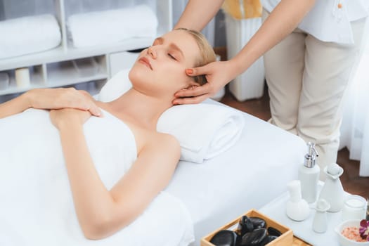 Caucasian woman enjoying relaxing anti-stress head massage and pampering facial beauty skin recreation leisure in dayspa modern light ambient at luxury resort or hotel spa salon. Quiescent