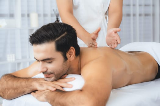 Caucasian man customer enjoying relaxing anti-stress spa massage and pampering with beauty skin recreation leisure in day light ambient salon spa at luxury resort or hotel. Quiescent