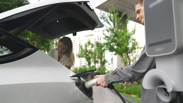 Young couple travel with EV electric car charging at green sustainable home in summer shows urban sustainability lifestyle by green clean rechargeable energy of electric vehicle innards