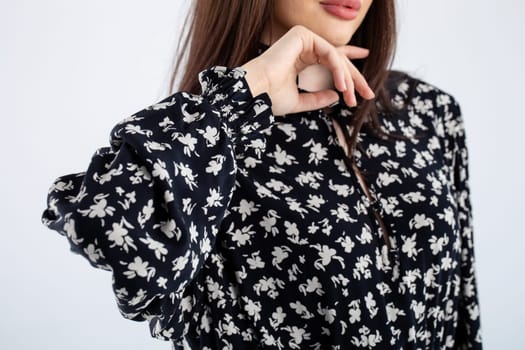 Portrait of a woman with long brown hair in a black floral blouse, looking serious at the camera with elegant style.