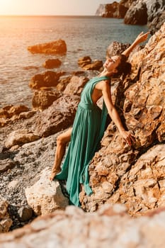 Woman green dress sea. Woman in a long mint dress posing on a beach with rocks on sunny day. Girl on the nature on blue sky background