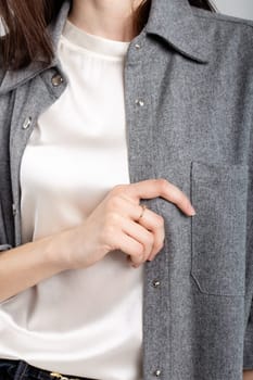 A stylish young woman in a gray shirt poses confidently with her hand in her pocket, showcasing modern fashion.
