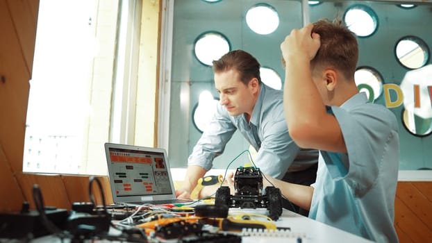 Caucasian teacher help student fixing car model and giving advise for programing system or coding prompt while highschool boy listen and use equipment to repair robot at STEM classroom. Edification.