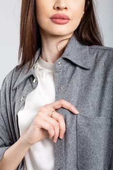 A stylish young woman in a gray shirt poses confidently with her hand in her pocket, showcasing modern fashion.