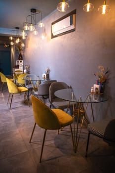 Cozy restaurant interior with glass tables, yellow chairs, textured walls, and pendant lights hanging from the ceiling.