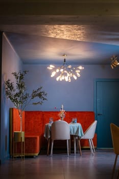 A beautiful restaurant interior with blue walls and red velvet furniture. The restaurant is lit by a beautiful chandelier.