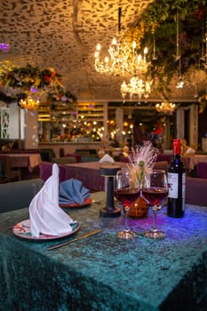 Elegant restaurant interior with round tables, purple tablecloths, chandeliers, and floral decor. Wine bottle on the table.