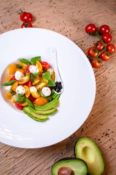 Healthy salad with tomatoes, avocado, mozzarella, basil on white plate. Garnished with balsamic glaze, served with bread.