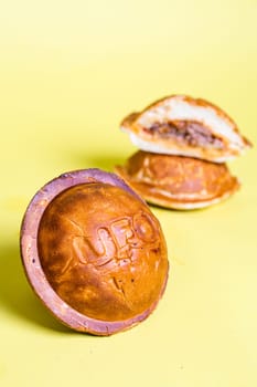 Round bread roll with UFO imprint, isolated on yellow background, split roll with meat filling stacked on top. Baked, tasty, delicious.