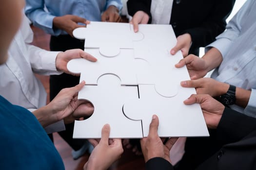 Diverse corporate officer workers collaborate in office, connecting puzzle pieces to represent partnership and teamwork. Unity and synergy in business concept by merging jigsaw puzzle. Concord