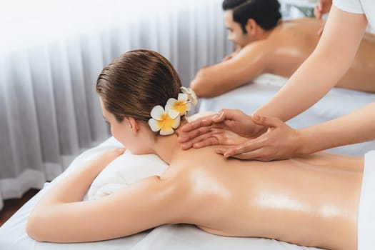 Caucasian couple customer enjoying relaxing anti-stress spa massage and pampering with beauty skin recreation leisure in day light ambient salon spa at luxury resort or hotel. Quiescent