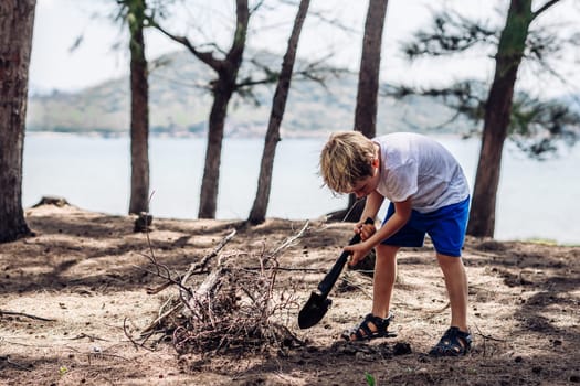 Cute boy digging soil in forest near sea beach. Family natural education skills. Travelling together. Learning camping organizing bonfire.
