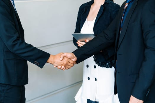 Business people agreement concept. Businessman do handshake with another businessman in the office meeting room. Young Asian secretary lady stands beside them. uds